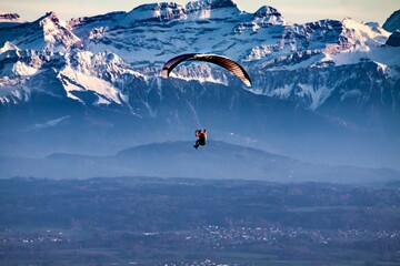 Naklejka na ściany i meble a person parasailing in the middle of a valley with snowy mountains in the background
