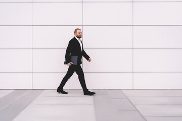 Serious businessman walking on street with folder