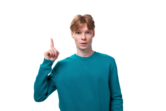 young caucasian student guy with red hair dressed in a blue sweater raised his thumb up on a white background with copy space