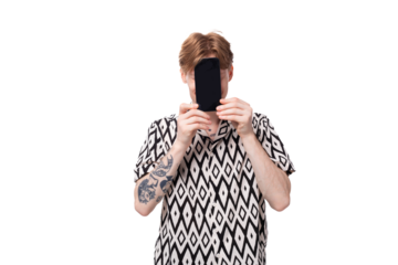 young smiling red-haired man dressed in a summer short-sleeved shirt in black and white holds a smartphone with a mockup