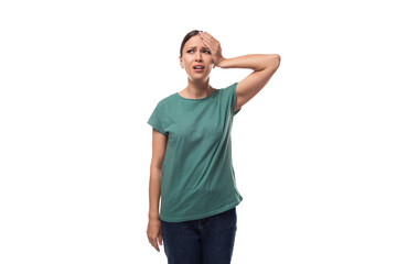 young forgetful brunette woman dressed in a green t-shirt on a white background - obrazy, fototapety, plakaty