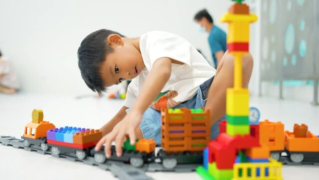 Adorable kindergarten 5 year boy playing color plastic block toy construction site building with transport industry