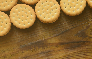A round sandwich cookie with coconut filling lies in large quantities on a brown wooden surface. Photo of edible treats on a wooden background with copy space