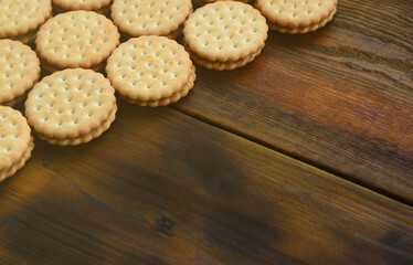 A round sandwich cookie with coconut filling lies in large quantities on a brown wooden surface. Photo of edible treats on a wooden background with copy space