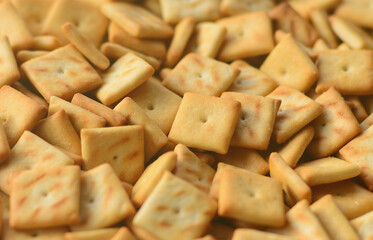 A lot of small cookies are square shaped. A pattern of a yellow salt cracker. Background image with salted pastry