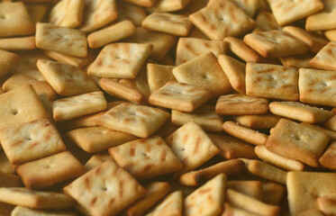 A lot of small cookies are square shaped. A pattern of a yellow salt cracker. Background image with salted pastry