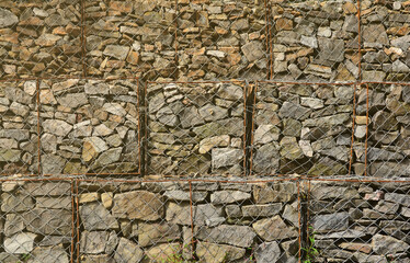 Photo of several gabions. The mesh cells of the cubic form are filled with mountain stones of various shapes that let water through the rain, but protect the road from falling stones