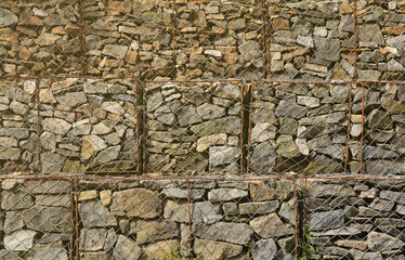 Photo of several gabions. The mesh cells of the cubic form are filled with mountain stones of...