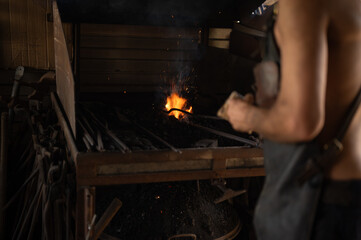 Unrecognizable blacksmith working with the furnace fire in his metal workshop.