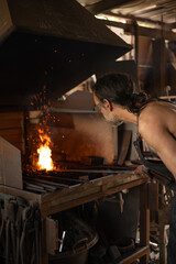 Metal workshop worker stoking a forge fire.