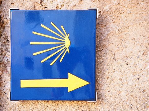 The way of st. James blue sign with yellow Shell and right arrow on a stone wall 