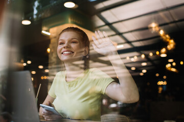 Cheerful woman waving hand in cafe