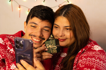 cheerful young couple making video call with their family on the cell phone showing a small gift on Christmas Eve