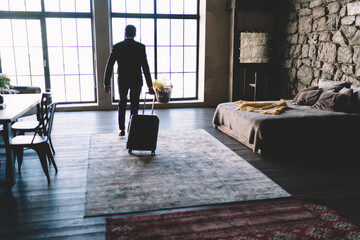 Anonymous traveler with suitcase in spacious hotel room