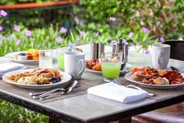 Gourmet breakfast spread on outdoor table with fresh pastries, juice, and coffee in tropical garden setting. Culinary travel and dining.