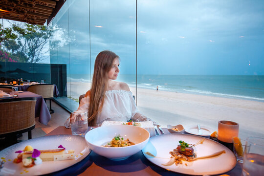Casual chic dressed female diner experiencing fine eating, tranquil beachside setting, sophisticated culinary delight.