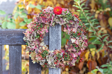 Blumenkranz mit Hortensienblüten, Efeubeeren und Hagebutten hängend an der Gartenbank
