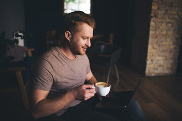 Focused man with cup of coffee working remotely on netbook