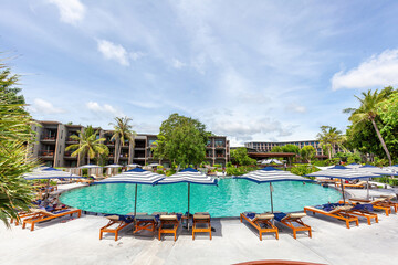 Spacious resort swimming area with guests, palm trees, sun loungers, and umbrellas in sunny ambiance. Travel and Leisure.