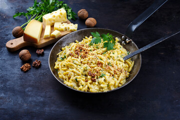 Traditionelle Allgäuer Käsespätzle mit Walnüssen serviert als Nahaufnahme in einer Eisenpfanne auf einem rustikalen Board 