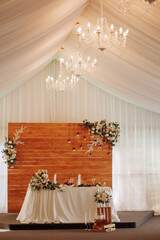 Elegant wedding table in a beige fabric tent with a chandelier, flowers and candles. The concept of a romantic and luxurious wedding celebration.