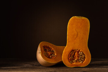 autumn vegetables. ripe raw pumpkin cut lengthwise in half lies on an old wooden table on a dark brown soft background with a light spot. butternut squash. side view with copy space