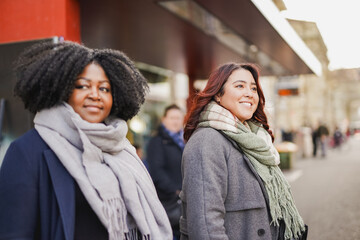 Multiracial young women waiting together at bus station in the city during winter time