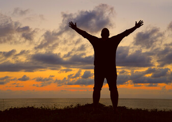 Fototapeta na wymiar black Silhouette of a man with raised-up arms at the sunset. Silhouette male raised hand in the air with success goal on sunset background. Man standing on top of coast. freedom life concept. hands up