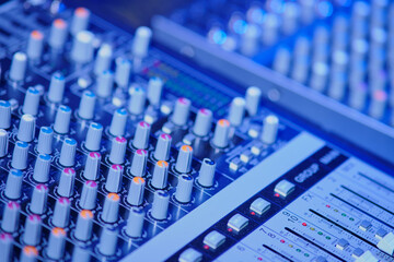 Audio mixing console, close-up, blue toned image.
