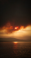 Fototapeta na wymiar Sol tapado por columna de humo en incendio junto al mar