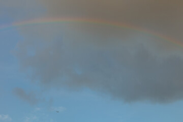 空にかかる大きな虹とその下を飛んでいく旅客機