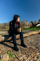 A woman sits on a felled tree and drinks coffee