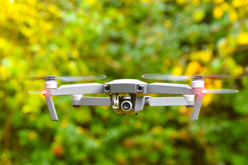 Drone with digital camera and fast rotating propellers flying taking video and pictures. Greenery...