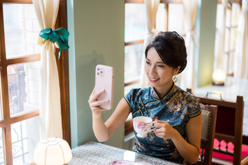 Woman wear traditional chinese cheongsam and use of mobile phone to take photo in the vintage restaurant