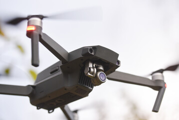 Drone quadcopter with digital camera and fast rotating propellers flying taking video and pictures. Greenery backgroud
