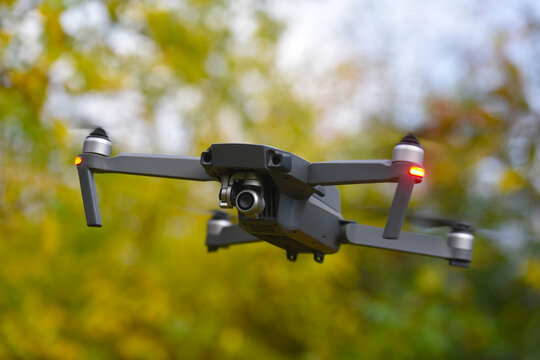 Drone with digital camera and fast rotating propellers flying taking video and pictures. Greenery backgroud
