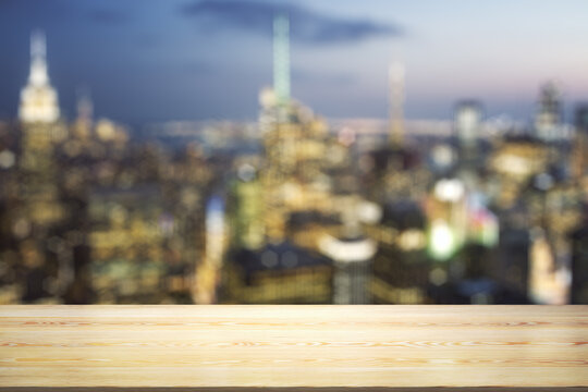 Empty wooden tabletop with beautiful blurry skyscrapers at evening on background, mock up