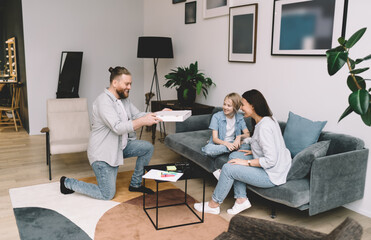 Positive man with pizza standing against sofa