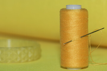 spool of yellow thread and needle on a yellow background.