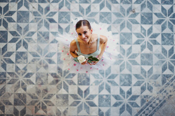 Portrait of a ballerina holding a white rose while standing on a colorful tiles