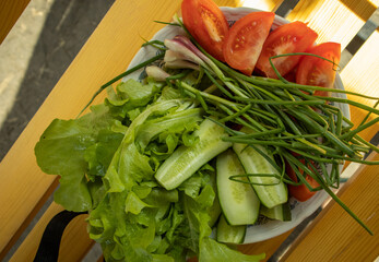 Fresh vegetables - lettuce, green onion, tomatoes and cucumbers on a white plate on a wooden background. The concept of cooking healthy food. View from above
