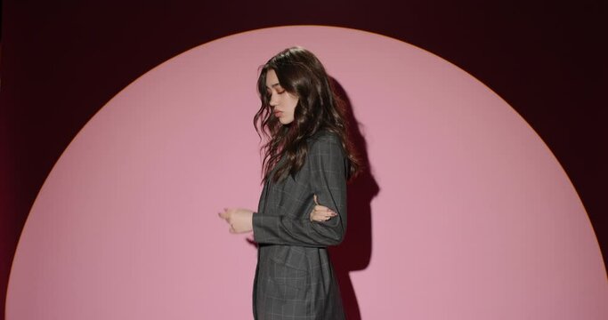 Backstage professional fashion photo shoot. Slow motion. Young girl model in black pantsuit posing in white light of cyclorama on pink-powdery color background. Modern people, young adult and youth