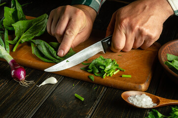 Chef hands cut spinach with a knife on a kitchen cutting board. Preparing vegetarian food in the kitchen. Vegetable diet concept