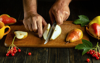 Close-up of a man's hands with a knife slicing ripe pears to serve on the table for dessert. - obrazy, fototapety, plakaty