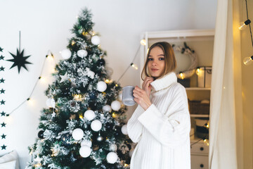 Happy woman with cup of hot drink near Christmas tree