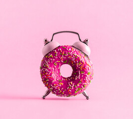 Creative art collage donut and alarm clock on pink background.