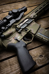 A modern carbine with an optical sight and a silencer. Weapons in camouflage coloring. Old wooden back