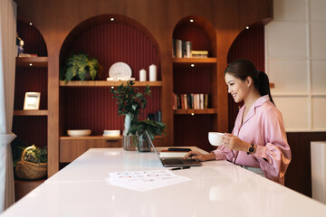 Businesswoman reading business chart on laptop and drinking hot tea while remote working at home.