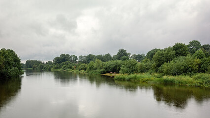 Fototapeta na wymiar Lithuanian river on the banks of green foliage, view on a cloudy day with light rain