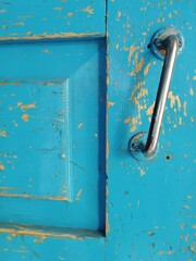Old wooden door with simple metal handle. Fragment of blue textured door. Close up detail shot. Handle on old wooden door. Rustic traditional culture